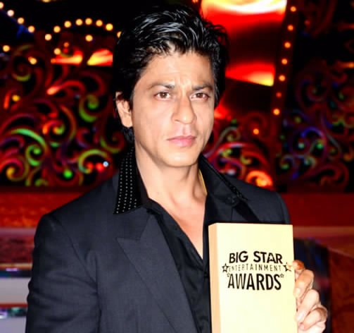Shah Rukh Khan wearing a dark blazer with a black shirt at an awards appearance
