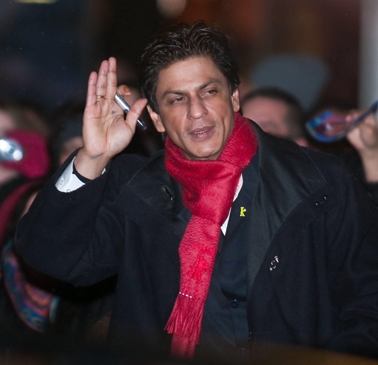 Shah Rukh Khan wearing a black coat with a bright red scarf