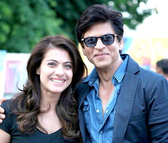 Shah Rukh Khan beside Kajol, wearing a blue open-collar shirt, dark blazer and sunglasses