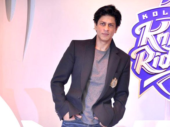 Shah Rukh Khan wearing a dark blazer with a grey T-shirt and blue jeans